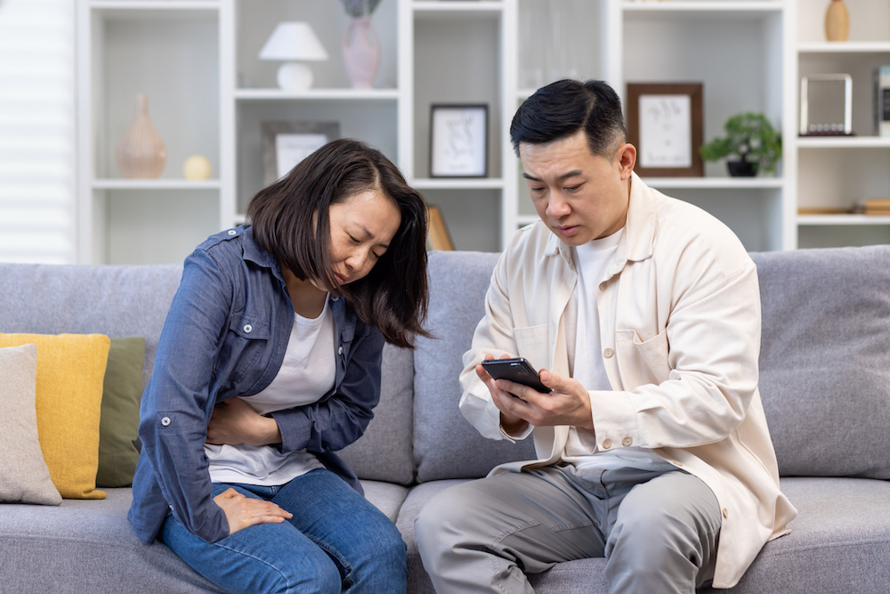 Wife holding side in pain and husband searching for "pain clinic near me" on his phone.